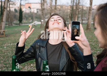 Frau machen Fotos von Freund balancing Flaschenverschlüsse auf Wangen Stockfoto