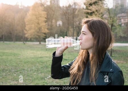 Junge Frau trinkt aus der Flasche Wasser im Park Stockfoto