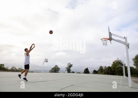 Männliche Jugendliche Basketballspieler wirft Ball in Richtung Basketballkorb Stockfoto