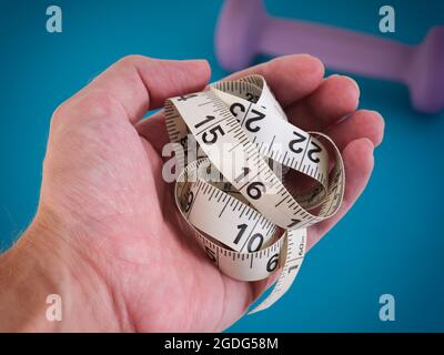 Eine Person, die ein Maßband hält, nachdem sie die Länge ihrer Taille nach dem Training überprüft hat. Nahaufnahme. Stockfoto