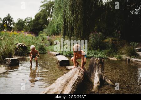 Kinder spielen im Sommer im Bach an Felsen und Baumstämmen im Wasser Stockfoto