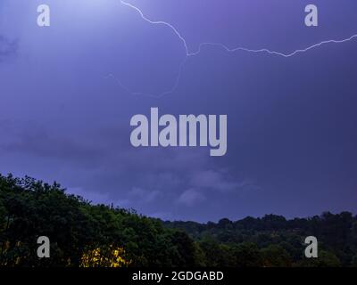 Blitzschlag über einem Hügel am Stadtrand - lange Belichtung in der Nacht Stockfoto