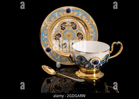 Luxus Gold Tee Party Kit. Tasse, Teller und Löffel. Isoliert auf schwarzem Hintergrund mit Reflexion. Souvenir-Geschenk mit traditionellen Mustern. Stockfoto