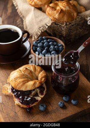 Croissant mit Heidelbeermarmelade und frischen Heidelbeeren auf einem rustikalen Holztisch Stockfoto