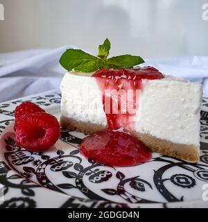 Stück Käsekuchen mit Himbeeren und Marmelade auf schwarzem und weißem Teller Stockfoto