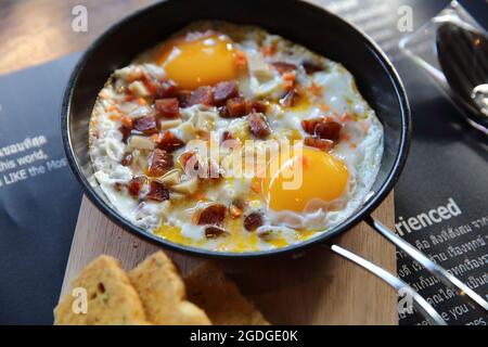 Frühstück mit gebratenen Eierspeisen mit heißer Pfanne und Brot Stockfoto