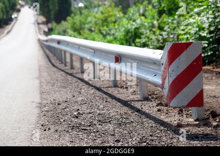 Rote Straßenreflektoren entlang der Straße. Metalleinzäunung von Barriere-Typ, Nahaufnahme. Straßen- und Verkehrssicherheit. Reflektierende Farbe auf dem Schild. Mittlere Barriere Stockfoto