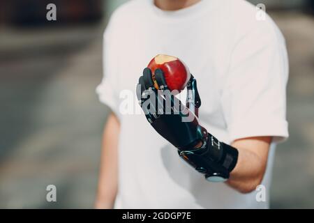 Junger behinderter Mann hält Apfelfrüchte mit künstlicher prothetischer Hand in legerer Kleidung Stockfoto