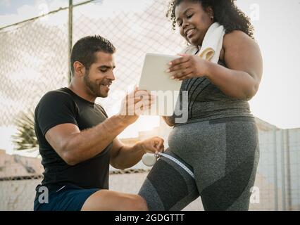 Personal Trainer, die mit einer kurvigen Frau arbeitet, die ihren Körper misst, während sie während der Trainingseinheit mit einem digitalen Tablet unterweisung Stockfoto