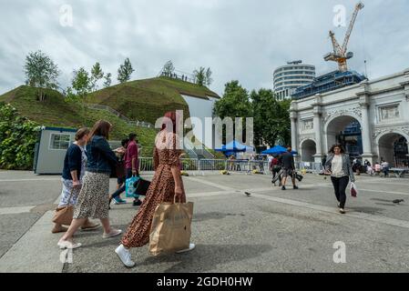 London, Großbritannien. August 2021. Die Menschen passieren den Marble Arch Mound. Melvyn Caplan, der stellvertretende Vorsitzende des Stadtrats von Westminster, ist zurückgetreten, nachdem die anfänglichen Kosten von 2 Mio. £für den Hügel jetzt auf 6 Mio. £geschätzt wurden. Der 25 m hohe künstliche Hügel wurde im Auftrag des rats von MVRDV Architekten als „das schlimmste Wahrzeichen Londons“ kritisiert. Derzeit steht der Hügel im August für einen Besuch frei, die Wiedereröffnung ist für September geplant. Kredit: Stephen Chung/Alamy Live Nachrichten Stockfoto