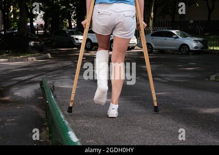 Eine Frau mit gebrochenem Bein geht mit orthopädischen Krücken eine Rampe hinunter. Stockfoto