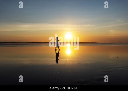 Kuta, Indonesien - 14. September 2018: Silhouette einer Frau, die am Seminyak-Strand auf Bali spazieren und den Sonnenuntergang genießen kann. Es ist eine der Touristenattraktionen in Stockfoto