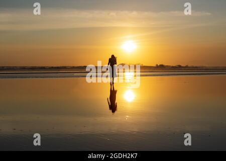 Kuta, Indonesien - 14. September 2018: Silhouette einer Frau, die am Seminyak-Strand auf Bali spazieren und den Sonnenuntergang genießen kann. Es ist eine der Touristenattraktionen in Stockfoto