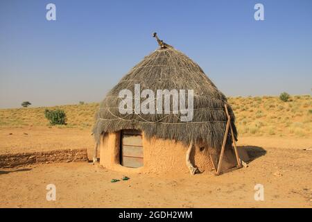 Ein Foto einer traditionellen reetgedeckten Lehm- und Schlammhütte und eines Hauses an einem klaren, sonnigen Tag am blauen Himmel in der Thar-Wüste in Rajasthan, Indien Stockfoto