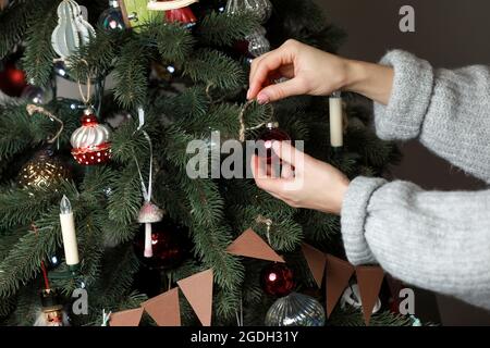 Die Hand der Frau schmückt den Weihnachtsbaum mit Weihnachts- und Neujahrsspielzeug. Weibliche Hand schmückt einen Weihnachtsbaum mit Kugeln. Neujahrsstimmung. Ch Stockfoto