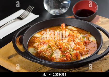 Garnelenauflauf mit Tomaten und Paprika in einer schwarzen Steinpfanne. Stockfoto