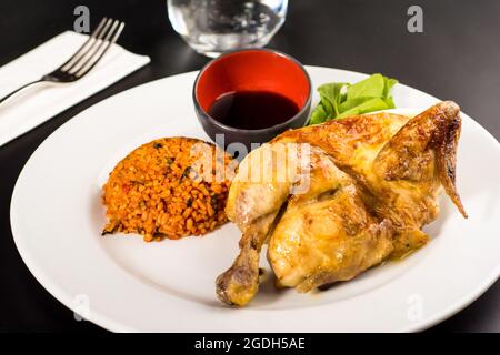 Gebratenes Huhn auf Holzkohle mit Bulgur-Pilaf auf einem weißen Porzellanteller gekocht. Stockfoto