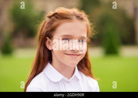 Foto von positiven fröhlich liebenswert niedlich Ingwer Schulmädchen aussehen Kamera Lächeln tragen weißes Hemd Uniform Park draußen Stockfoto