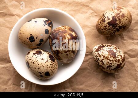 Mehrere Bio-Wachteleier mit einer weißen Untertasse auf braunem Papier, Nahaufnahme, Draufsicht. Stockfoto