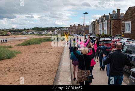 North Berwick, East Lothian, Schottland, Großbritannien 13. August 2021. Silent Adventures Disco: Eine Gruppe von fröhlichen Festivalbesuchern wird durch die Küstenstadt zum Strand geführt und singt und tanzt Musik über Kopfhörer Stockfoto