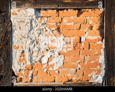 Detailansicht einer Fachwerkwand mit freiliegenden Ziegeln und Zementflecken im Licht der Abendsonne. Stockfoto