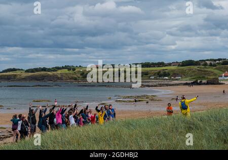 North Berwick, East Lothian, Schottland, Großbritannien 13. August 2021. Silent Adventures Disco: Eine Gruppe von fröhlichen Festivalbesuchern wird durch die Küstenstadt zum Strand geführt und singt und tanzt Musik über Kopfhörer Stockfoto