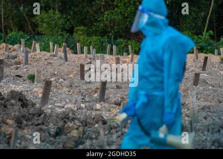 Kuala Lumpur, Malaysia. August 2021. Ein Arbeiter mit Schutzanzug geht auf einem Friedhof in Selangor, Malaysia, 13. August 2021. Malaysia verzeichnete 21,468 neue COVID-19-Infektionen, teilte das Gesundheitsministerium am Freitag mit und brachte damit die landesweite Gesamtzahl auf 1,363,683. Quelle: Chong Voon Chung/Xinhua/Alamy Live News Stockfoto