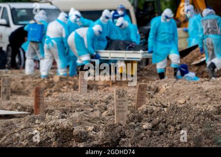 Kuala Lumpur, Malaysia. August 2021. Arbeiter in Schutzanzügen tragen den Leichnam eines COVID-19-Opfers auf einem Friedhof in Selangor, Malaysia, 13. August 2021. Malaysia verzeichnete 21,468 neue COVID-19-Infektionen, teilte das Gesundheitsministerium am Freitag mit und brachte damit die landesweite Gesamtzahl auf 1,363,683. Quelle: Chong Voon Chung/Xinhua/Alamy Live News Stockfoto