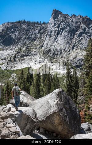 Ein Mann wandert auf dem Tokopah Falls Trail und geht auf große Felsbrocken mit Blick auf das gletschergeschnitzte Tal und die Granitkuppel des Wachtturms bei Sequoia Na Stockfoto