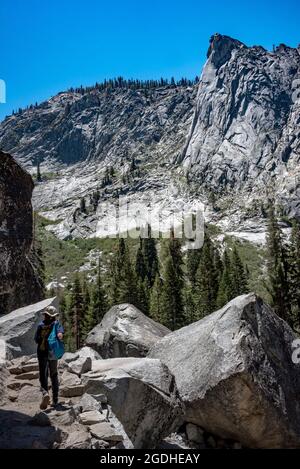 Ein junger Wanderer folgt dem Tokopah Falls Trail, vorbei an Granitfelsen mit einem weiten Blick über das Tokopah Valley und die Granitkuppel des Wachtturms. Stockfoto