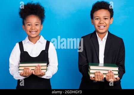 Foto von glücklichen positiven dunklen Haut Kinder Schüler halten Materialien Bücher lächeln isoliert auf blauem Hintergrund Stockfoto