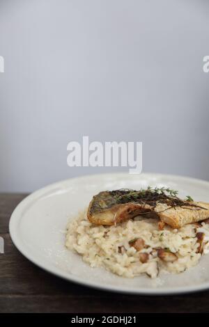 Risotto mit Seebarsch-Filetsteak auf Holzhintergrund, italienische Küche Stockfoto