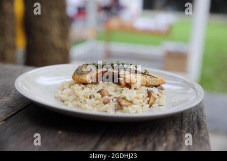 Risotto mit Seebarsch-Filetsteak auf Holzhintergrund, italienische Küche Stockfoto