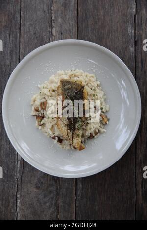 Risotto mit Seebarsch-Filetsteak auf Holzhintergrund, italienische Küche Stockfoto
