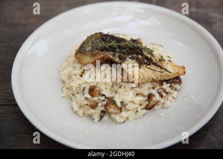 Risotto mit Seebarsch-Filetsteak auf Holzhintergrund, italienische Küche Stockfoto