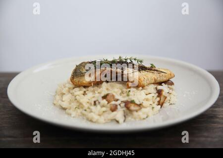 Risotto mit Seebarsch-Filetsteak auf Holzhintergrund, italienische Küche Stockfoto