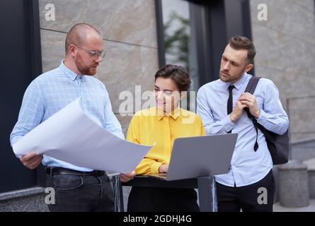 Geschäftsleute, Architekten oder Designer Team-Konzept. Männer und Frauen stehen draußen, nutzen Laptops und diskutieren Design, zeigen Baupläne, sprechen und Brainstorming. Hochwertige Fotos Stockfoto