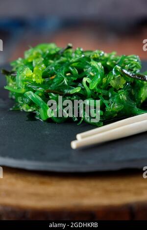 Wakame-Algensalat mit Sesam auf schwarzem Teller und Holztisch Stockfoto