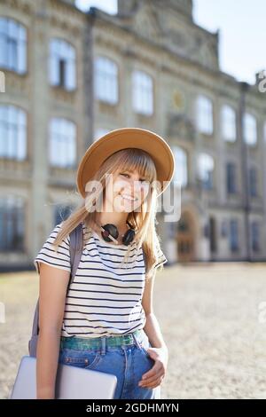 College-Mädchen, Studentenportrait, Studium im Ausland oder Bildungskonzept. Fröhlich lächelnd junge blonde europäische Universitäts- oder Hochschulstudentin mit braunem Hut auf dem Campus. Hochwertige Bilder Stockfoto