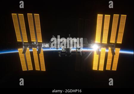 Die Internationale Raumstation (ISS) gegen die dunkle Erde mit der aufgehenden Sonne dahinter Stockfoto