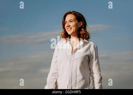 Glückliche Frau in einem weißen Hemd. Porträt vor einem blauen Himmel. Glück und Gesundheit Konzept Stockfoto