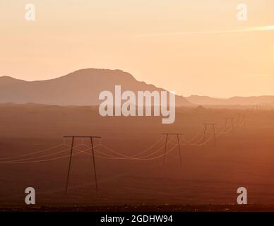 Moderne Strommasten mit Drähten im Tal in der Nähe von Bergen bei Sonnenaufgang in Island Stockfoto