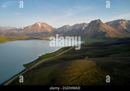 Malerischer Blick auf den ruhigen, sauberen See und die schneebedeckten Berge, die sich vor dem blauen Morgenhimmel in Island befinden Stockfoto