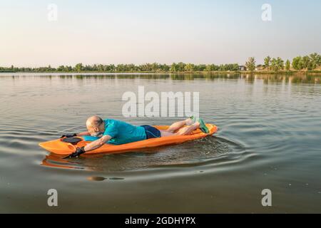 Der sportliche, ältere Mann paddelt ein gestrecktes Kajak auf einem See in Colorado, dieser Wassersport kombiniert Aspekte des Kajakfahrens und Schwimmens Stockfoto