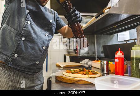 Closeup Hand des Chef-Bäcker in weißer uniform schneiden Pizza in der Küche Stockfoto