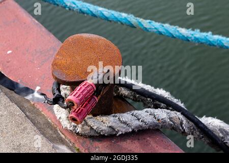 Ein Seil und ein elektrisches Kabel mit Klemmen auf einem Poller im Hafen. Stockfoto