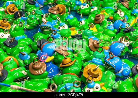 Kinderspiel Entenfischen auf einem Jahrmarkt. Viele grüne und blaue Plastikfrösche und Plastikenten in einem Wasserbecken mit einem Ring zum Angeln auf der Luftröhre Stockfoto