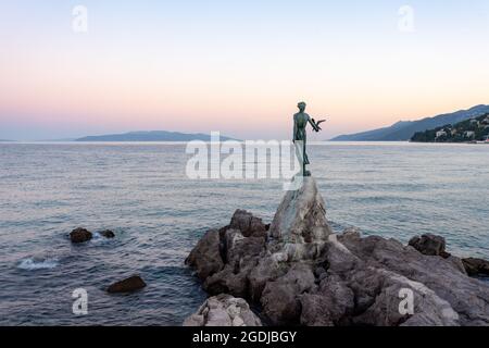 'Maid with a Seagull', eine beliebte Statue, die auf einem Felsen in der Nähe der Küstenpromenade des kroatischen Badeortes Opatija steht. Abendaufnahme. Stockfoto