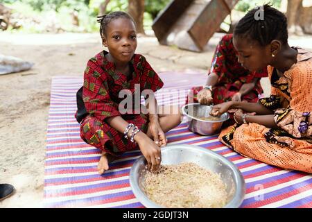 Kleines schwarzes afrikanisches Mädchen mit einem vollen Mund, das ihr Essen genießend kaut Stockfoto