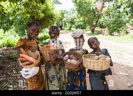 Vier intelligente junge afrikanische Mädchen mit Strohkörben voller Gemüse auf dem Weg zum lokalen Markt Stockfoto